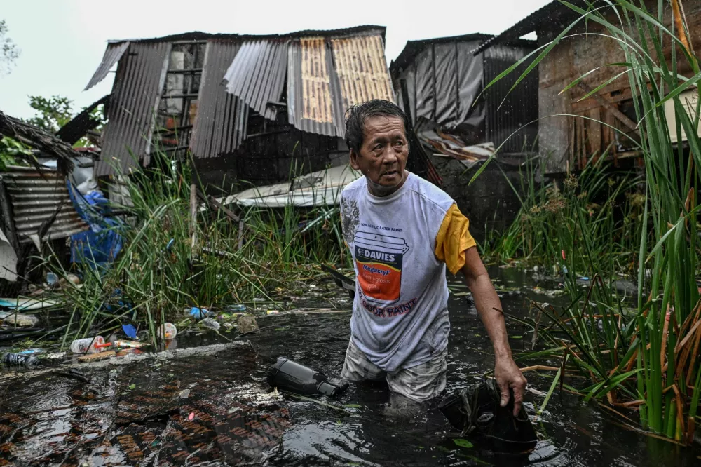 Ceverino Macob, 64, wades through the flood as he recovers a roof blown from his house (seen in the background) due to strong winds after Typhoon Fung-wong hit Dagupan City, Pangasinan, Philippines, November 10, 2025. REUTERS/Noel Celis