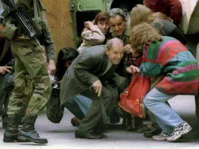 Hitchhikers, who were riding in the rear of a locked transit van which came under sniper fire in Sarajevo, take cover behind a French armoured personnel carrier after a French UN soldier (L) let them out in a June 7, 1995 file photo. Slobodan Milosevic, branded the "butcher of the Balkans" for the wars that tore Yugoslavia apart in the 1990s, was found dead in his cell on March 12, 2006 just months before his trial was expected to conclude. "Milosevic was found lifeless on his bed in his cell," the UN war crimes tribunal in The Hague said in a statement.  REUTERS/Chris Helgren/Files