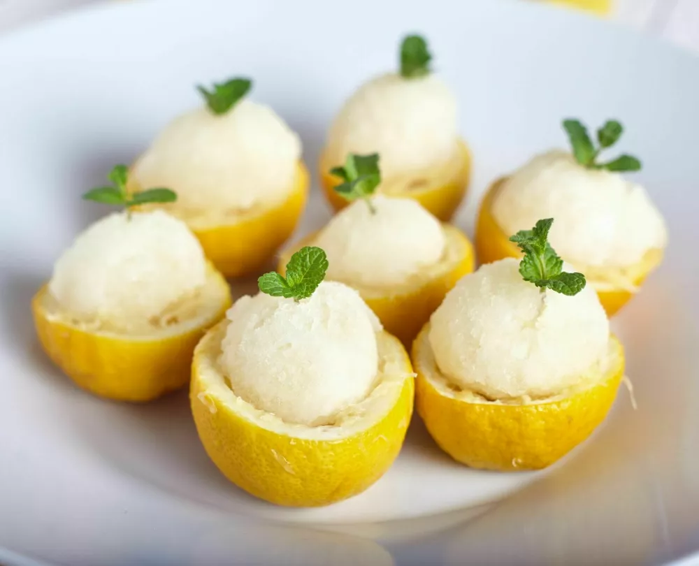 Lemon sorbet or ice cream inside fresh lemons decorated with mint leaves on big white plate / Foto: Alexbai
