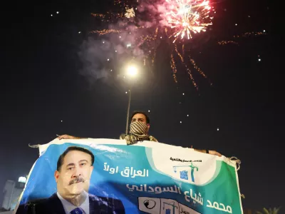 A man holds an election poster featuring current Prime Minister Mohammed Shia' al-Sudani, with fireworks in the background, as supporters of the Reconstruction and Development Coalition celebrate after preliminary election results were announced in Baghdad, Iraq, November 12, 2025. REUTERS/Ahmed Saad