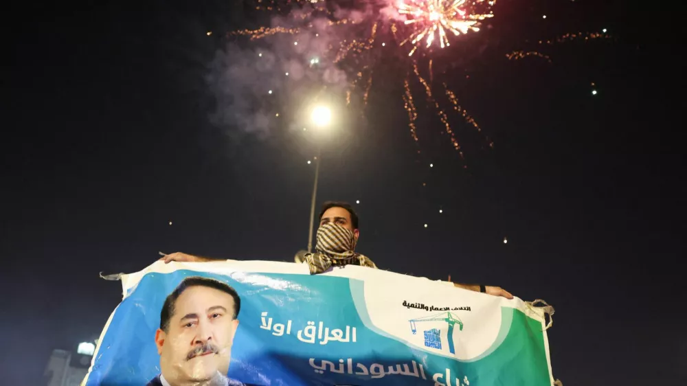 A man holds an election poster featuring current Prime Minister Mohammed Shia' al-Sudani, with fireworks in the background, as supporters of the Reconstruction and Development Coalition celebrate after preliminary election results were announced in Baghdad, Iraq, November 12, 2025. REUTERS/Ahmed Saad