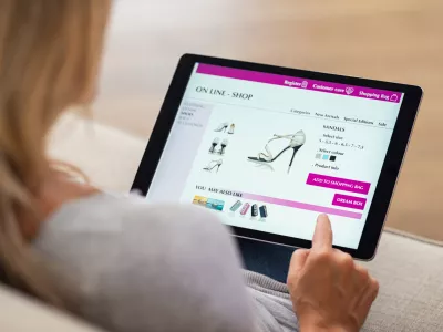 ﻿Closeup of woman doing online shopping on digital tablet at home. Rear view of woman hand touching screen while selecting shoes on ecommerce portal. Lady use e-commerce webshop to buy shoes.