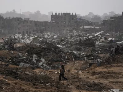 A Palestinian woman walks through a rainstorm past buildings destroyed in Israeli strikes in the Sheikh Radwan neighborhood of Gaza City, Friday, Nov. 14, 2025. (AP Photo/Jehad Alshrafi)