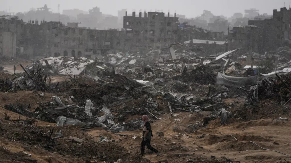 A Palestinian woman walks through a rainstorm past buildings destroyed in Israeli strikes in the Sheikh Radwan neighborhood of Gaza City, Friday, Nov. 14, 2025. (AP Photo/Jehad Alshrafi)