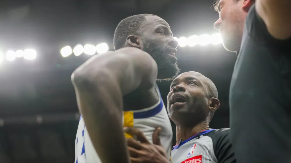 Golden State Warriors forward Draymond Green (23) is held back by referee Courtney Kirkland while talking to New Orleans Pelicans fan Sam Green during the first half of an NBA basketball game against the New Orleans Pelicans in New Orleans, Sunday, Nov. 16, 2025. (David Grunfeld/The Times-Picayune via AP)