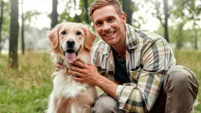 A cheerful man enjoys a delightful moment with his playful golden retriever in a lush forest, capturing joy and companionship in nature, ideal for pet lovers and outdoor enthusiasts
