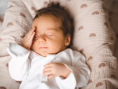 Infant baby boy 2-3 months old with headache and pain touching head in bed closeup. Childhood. Good morning.
