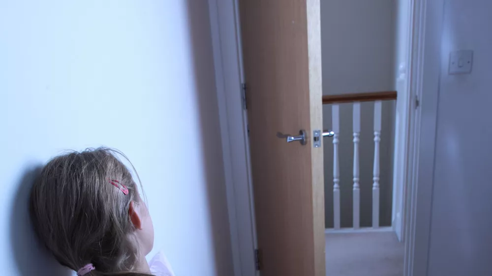 teenage girl sitting alone on her bed, back to camera.