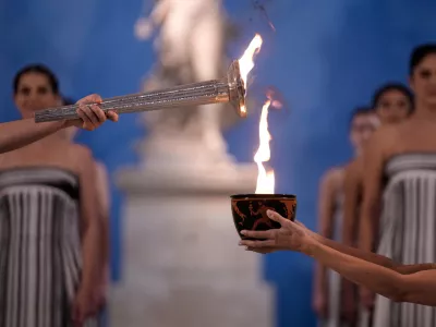 High Priestess Mary Mina, left, lights a torch from the Olympic flame during the flame lighting ceremony for the Milan Cortina 2026 Winter Olympics, at the archaeological museum of Olympia, Greece, Wednesday, Nov. 26, 2025. (AP Photo/Thanassis Stavrakis)