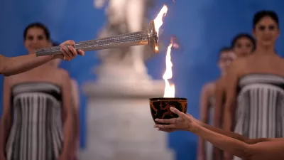 High Priestess Mary Mina, left, lights a torch from the Olympic flame during the flame lighting ceremony for the Milan Cortina 2026 Winter Olympics, at the archaeological museum of Olympia, Greece, Wednesday, Nov. 26, 2025. (AP Photo/Thanassis Stavrakis)