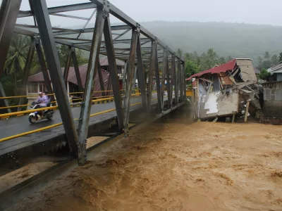Motorists ride on a bridge past buildings damaged by flooding in Tanah Datar, West Sumatra, Indonesia, Friday, Nov. 28, 2025. (AP Photo/Ali Nayaka)
