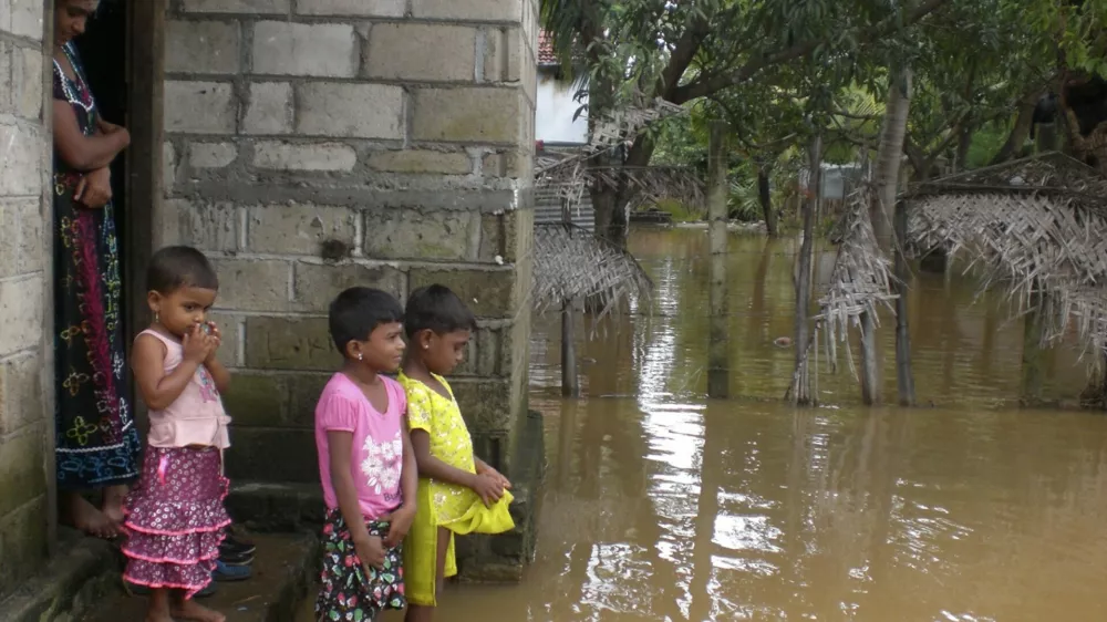 A family stands near their flooded home in Batticaloa district, about 320 km (199 miles) east of Colombo, February 6, 2011. Heavy rain triggered flooding in Sri Lanka that killed at least eleven people and is threatening up to 90 percent of the island nation's staple rice crop, heightening concerns over supply shocks and higher inflation, officials said on Sunday. REUTERS/Stringer (SRI LANKA - Tags: DISASTER ENVIRONMENT)
