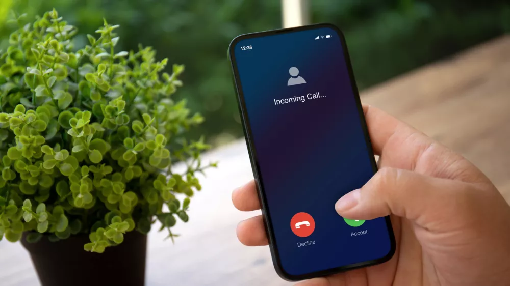 man hands holding phone with incoming call on screen in green cafe / Foto: Prykhodov