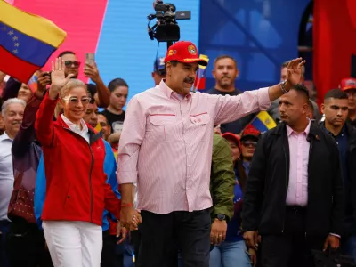 Venezuela's President Nicolas Maduro waves while holding the hand of his wife Cilia Flores during a ceremony to swear in new community-based organisations, as U.S. President Donald Trump's administration ramps up pressure on Maduro's government, in Caracas, Venezuela, December 1, 2025. REUTERS/Leonardo Fernandez Viloria