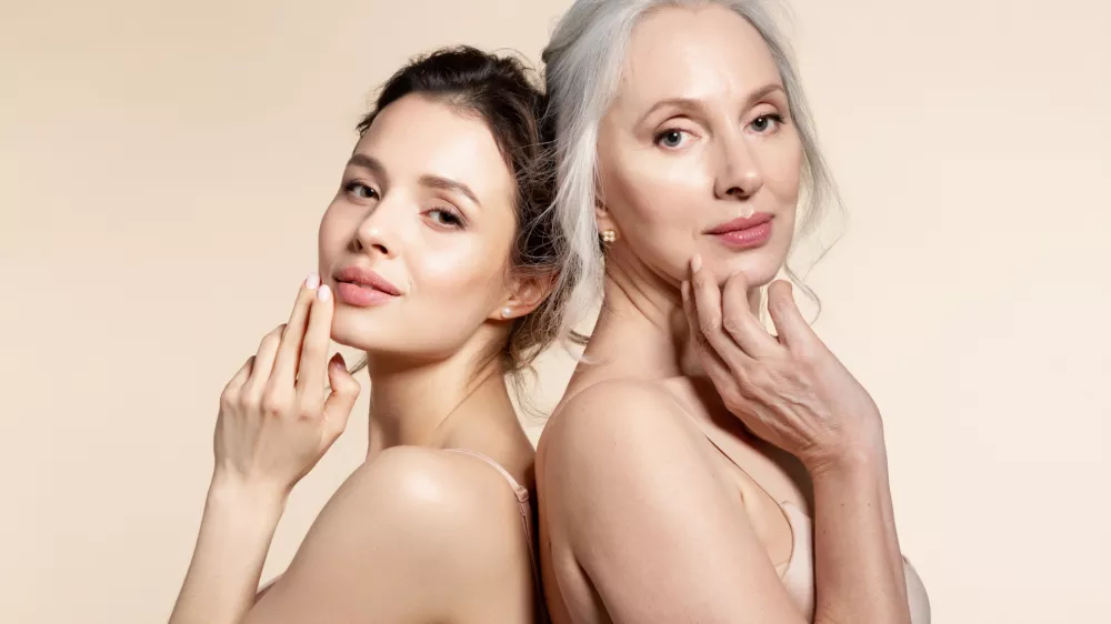 Elderly and young women with smooth skin and natural makeup standing back-to-back. Thinking, planning, dreaming