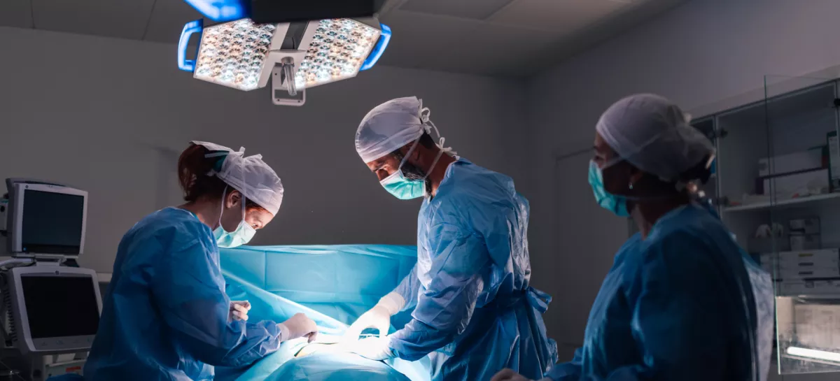 An intricate surgical procedure in progress with healthcare professionals in full surgical gear, under bright operating room lights, emphasizing the modern medical equipment and organization. / Foto: Zamrznutitonovi