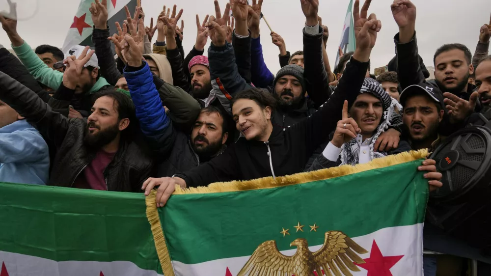 People celebrate and wave Syrian flags as they wait for a parade by the new Syrian army during celebrations marking the first anniversary of the ousting of former President Bashar Assad in Damascus, Syria, Monday, Dec. 8, 2025. (AP Photo/Hussein Malla)