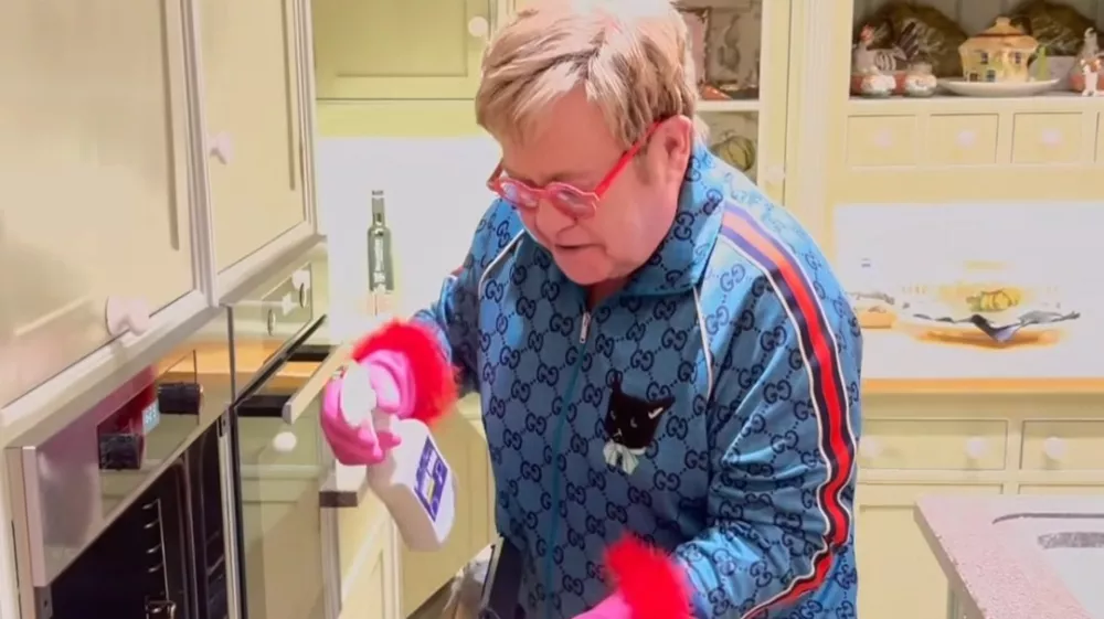 Sir Elton, znan po svojem ekscentričnem slogu oblačenja, je za či&scaron;čenje kuhinje oblekel modro trenerko, prekrito z logotipom znamke in mačjim motivom, v&scaron;itim na sprednji strani. F IG/posnetek zaslona 