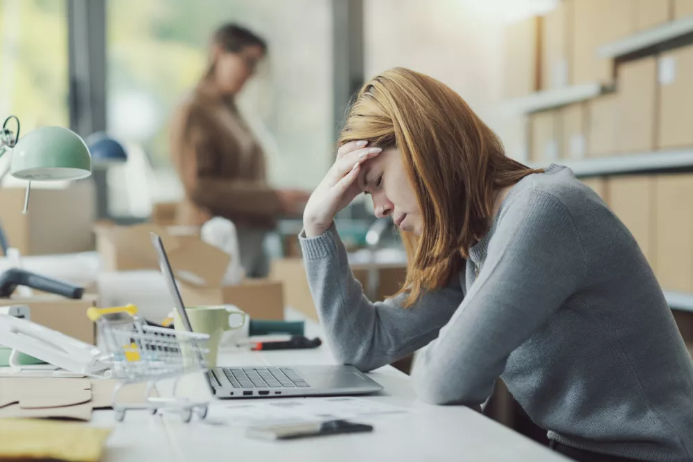 Exhausted woman sitting at the office desk and touching her head, she has a headache