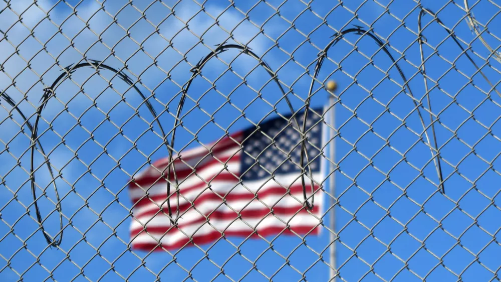 FILED - 15 January 2023, Cuba, Guant?namo: A U.S. flag flies behind barbed wire at the Guant?namo Bay naval base in Cuba. The US government flew 177 deportees from Guantanamo Bay to Honduras on 20 February. US border protection agency ICE said the deportees were then picked up and returned home by the Venezuelan government. Photo: Magdalena Miriam Tr?ndle/dpa