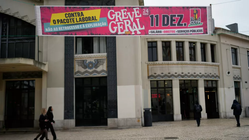 People walk past a banner calling for a general strike during a nationwide walkout to protest a new labour package announced by the centre-right government in Lisbon, Thursday, Dec. 11, 2025. (AP Photo/Armando Franca)