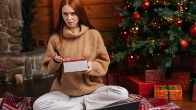 Dissatisfied young woman waiting for good Christmas present, lady with disappointment opening box with surprise on background of xmas tree at living room. Female looking at camera incomprehensibly.