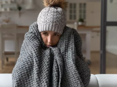 Dull young hispanic woman save herself from freezing wear winter clothes muffle up in blanket think of buying radiator heater. Shivering young lady sit on sofa in plaid ponder on much too cold at home / Foto: Fizkes