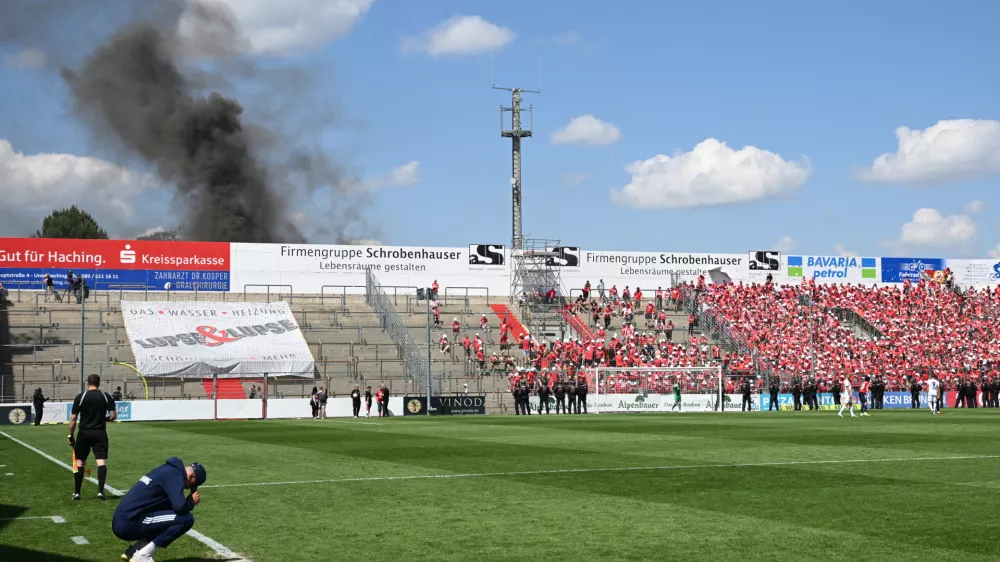 FILED - 11 June 2023, Bavaria, Unterhaching: Unterhaching coach Sandro Wagner (L) sits on the edge of the pitch while thick smoke rises behind the north stand during the the Regionalliga promotion round to the 3rd division soccer match between SpVgg Unterhaching and Energie Cottbus at Sportpark Unterhaching. The Bild paper said the council of the municipality of Unterhaching near Munich has given the green light to sell its 15,000-seat Sportpark Unterhaching stadium to Bayern for &middot;7.25 million ($8.5 million). Photo: Angelika Warmuth/dpa