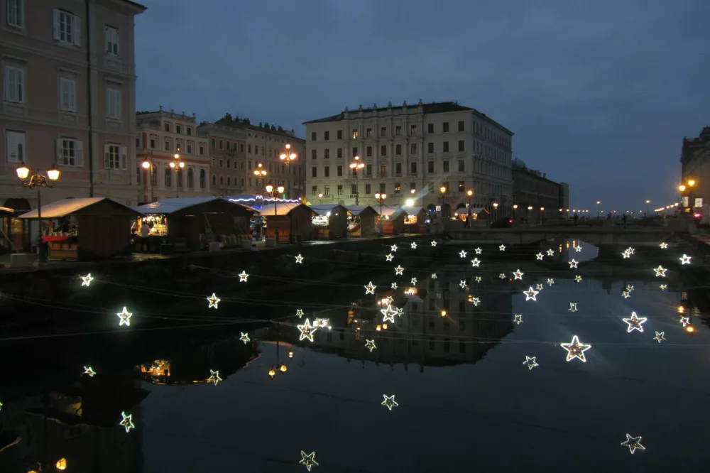  Predvečerne adventne zvezdice nad Canalom Grande, nekoč glavna reka v solinah, in zadaj Ponte Rosso, legendarni trg v centru Trsta, kjer stojnice s ponudniki iz Italije in Avstrije (slovenske ni), precej večje od ljubljanskih, ponujajo hrano in pijačo ter tipične decembrske sla&scaron;čice z zmernimi cenami.