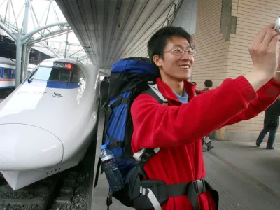 A traveler takes a snapshot of him with a bullet train in the backdrop at the train station in Beijing Wednesday, April 18, 2007. Faster Chinese trains running at about 200 kph (124 mph) began service Wednesday as part of a bid to keep up with ballooning transport demand, state media reported. (AP Photo/EyePress) ** CHINA OUT **
