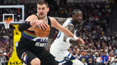 Denver Nuggets center Nikola Jokić, front, dribbles past Minnesota Timberwolves center Julius Randle in the first half of an NBA basketball game, Thursday, Dec. 25, 2025, in Denver. (AP Photo/David Zalubowski)