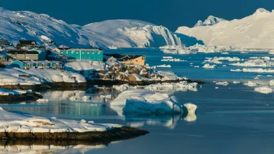 Colorful houses line the shores of a serene bay in the Arctic, surrounded by icebergs and snow-covered mountains, reflecting the warm glow of the sunset on the water.