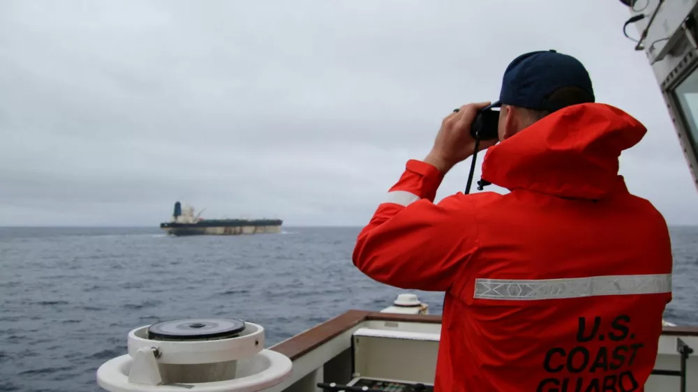 A U.S. Coast Guard official looks through binoculars at the ship Marinera (Ex-Bella 1) in this handout image released January 7, 2026. US EUROPEAN COMMAND via X/Handout via REUTERS  THIS IMAGE HAS BEEN SUPPLIED BY A THIRD PARTY. MANDATORY CREDIT. Verification lines: Reuters was not able to independently verify the location or the date when the photos were taken. But a U.S. official told Reuters the United States had pursued the tanker for more than two weeks across the Atlantic. Searches for the images found they had not appeared online before. The identity of the oil tanker was confirmed by the structures on the deck and bridge which matched file imagery.