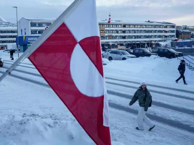 A woman walks on a street in front of a national flag in Nuuk, Greenland, on Wednesday, Jan. 14, 2026. (AP Photo/Evgeniy Maloletka)