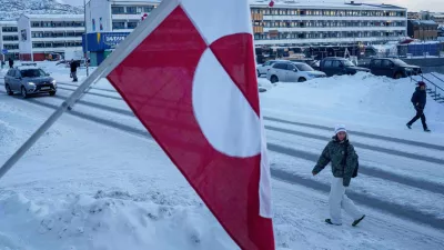 A woman walks on a street in front of a national flag in Nuuk, Greenland, on Wednesday, Jan. 14, 2026. (AP Photo/Evgeniy Maloletka)