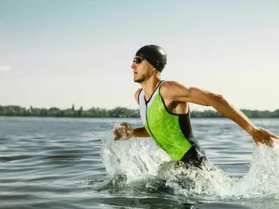Professional triathlete swimming in river's open water. Man wearing swim equipment practicing triathlon on the beach in summer's day. Concept of healthy lifestyle, sport, action, motion and movement. / Foto: Master1305