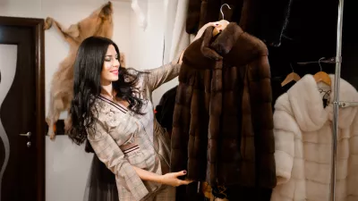 Attractive young woman in fur coat shop with a fur coats on the hanger