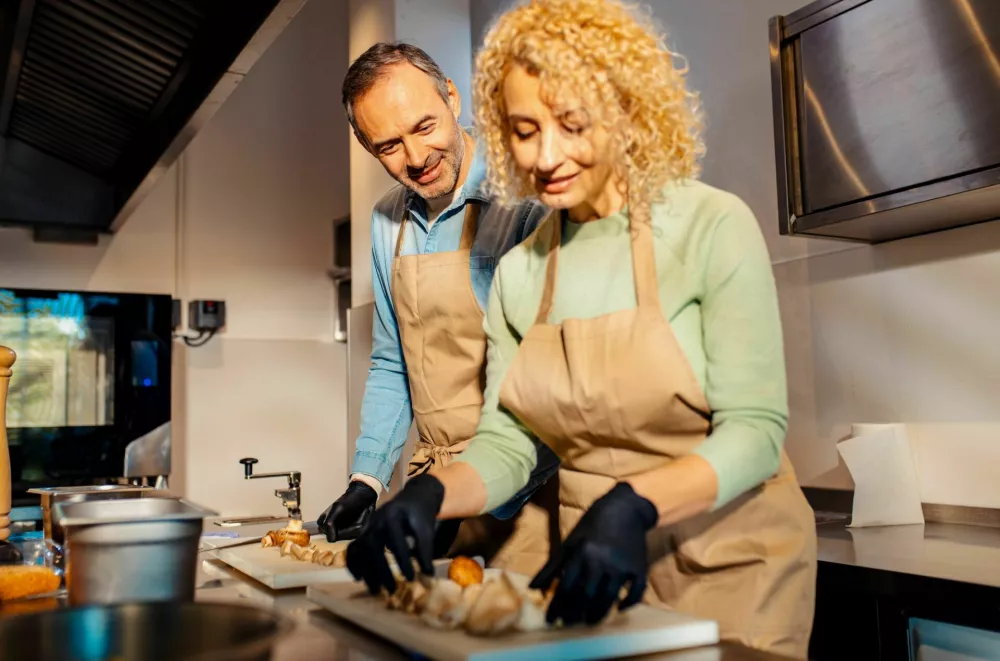 Middle-aged couple enjoying a cooking class with a chef preparing mushrooms for a meal in the kitchen. / Foto: Zoran Zeremski