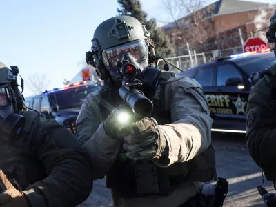 A Law enforcement member holds a weapon as they stand guard while people protest outside the Bishop Henry Whipple Federal Building, after the fatal shootings of Renee Nicole Good and Alex Pretti by federal immigration agents, in Minneapolis, Minnesota, U.S., January 30, 2026. REUTERS/Shannon Stapleton   TPX IMAGES OF THE DAY