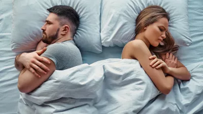 Young beautiful couple lying in bed turned back to back, arms crossed in anger and resentment. Relationship problems.Top view. / Foto: Harbucks