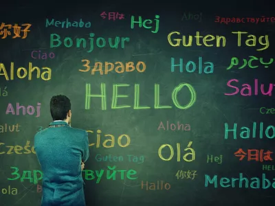 Rear view of a puzzled businessman in front of a huge chalkboard written with the word hallo in different languages and colors. Opportunity for learning many languages for students. / Foto: Bulat Silvia