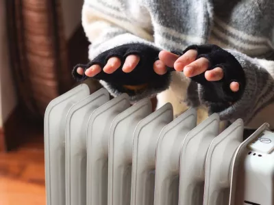 Person heating their hands at home over a domestic portable radiator in winter
