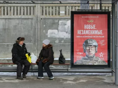 People sit at a bus stop next to a poster promoting contract military service in the Russian army's unmanned systems forces, in the Black Sea resort city of Yevpatoriya, Crimea February 9, 2026. REUTERS/Alexey Pavlishak