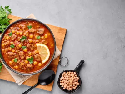 Moroccan Harira Soup in black bowl at grey concrete table top. Harira is Moroccan Cuisine dish with lamb or beef meat, chickpeas, lentils, tomatoes, ciliantro. Ramadan Iftar Food. Copy space. Top view / Foto: Andrei Kravtsov
