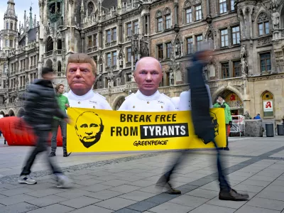 13 February 2026, Bayern, M&uuml;nchen: Greenpeace activists display giant sculptures of US President Donald Trump and Russian President Vladimir Putin standing on a 10-meter model gas tanker labeled "Fossil Gas" at Marienplatz in Munich. A banner reading "Break Free From Tyrants" accompanies the protest, marking the start of the Munich Security Conference. Photo: Malin Wunderlich/dpa