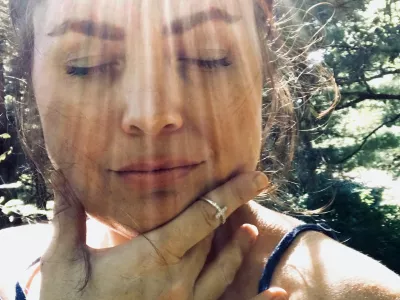 Beautiful middle aged woman, a portrait shot of face only, model is outside in the sun, with very distinct rays of sunlight making dramatic ray marks on her face. Her eyes are closed in relaxation and happiness, feeling the warmth. Model has dark brown, upswept hair and an off the shoulder top. / Foto: Jamie Casper