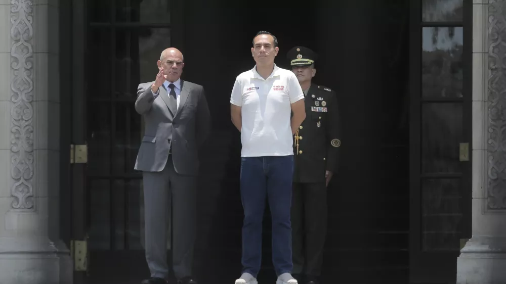 Photographed through a gate, Peru's President Jose Jeri, right, stands with Prime Minister Ernesto Alvarez during the changing of the guard ceremony at the government palace in Lima, Peru, Tuesday, Feb. 17, 2026. (AP Photo/Gerardo Marin)