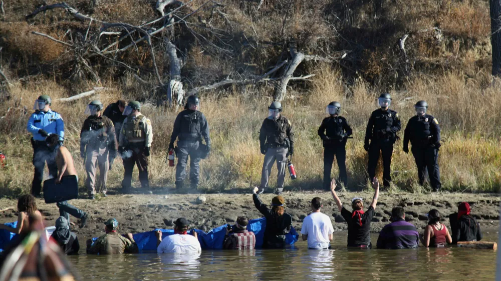 FILE - In this Nov. 2, 2016 file photo, protesters demonstrating against the expansion of the Dakota Access Pipeline wade in cold creek waters confronting local police as remnants of pepper spray waft over the crowd near Cannon Ball, N.D. (AP Photo/John L. Mone, File)