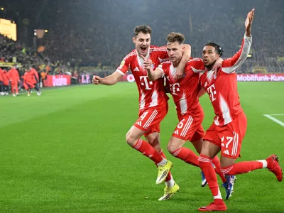 Bayern Munich's Joshua Kimmich, centre, celebrates with Josip Stanisic and Michael Olise after scoring his side's third goal during the Bundesliga soccer match between Borussia Dortmund and FC Bayern Munich in Dortmund, Germany, Saturday Feb. 28, 2026. (Federico Gambarini/dpa via AP)