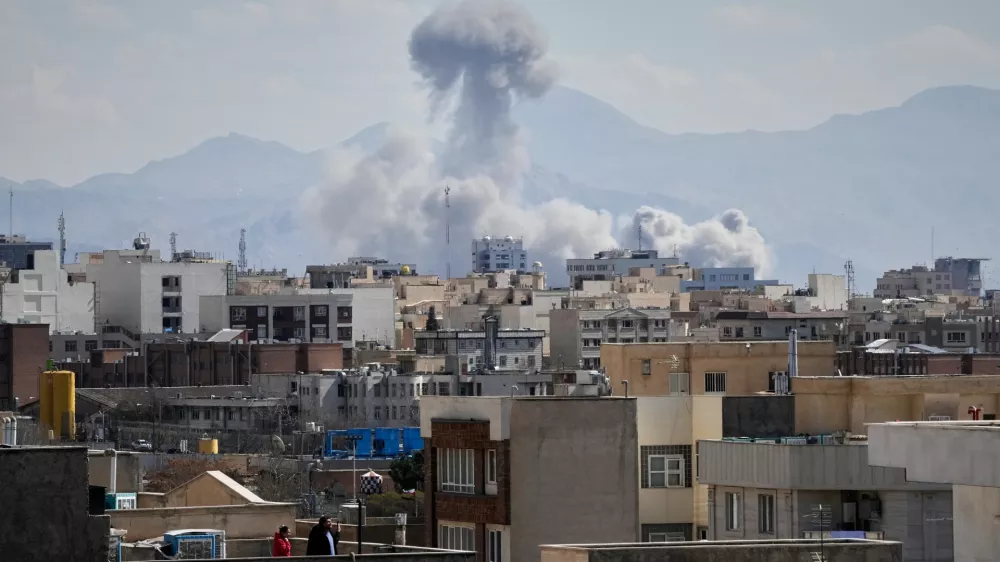 People watches from rooftop as a plume of smoke rises after a strike in Tehran, Iran, Sunday, March 1, 2026. (AP Photo/Vahid Salemi)